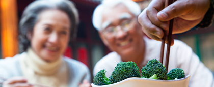 bowl of broccoli, chopsticks, smiling man and woman in background