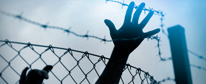 hand reaches over chain link fence and barbed wire