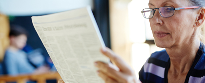 woman in glasses reads a newspaper