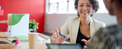 smiling woman at a work table talks with a colleague