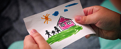 child holds drawing of house and family
