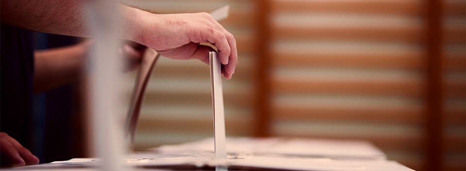 hands putting votes into a ballot box