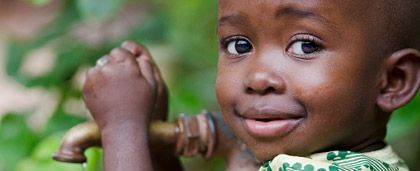 smiling little kid standing by a water spigot