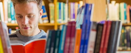 young adult reads a journal in a library