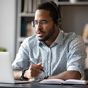 man with beard talking, with headset and laptop computer