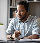 man with beard talking, with headset and laptop computer