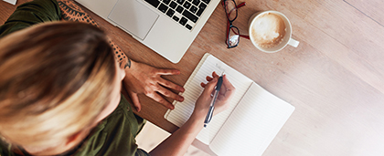 woman writing in notebook with laptop nearby