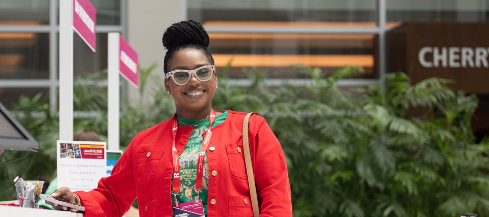 An attendee checks in at the registration area during the NASW National Conference, smiling while holding a phone and wearing an event badge