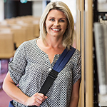 smiling woman stands leaning against library stacks