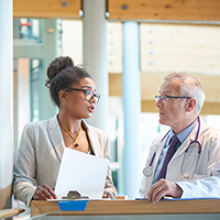 a woman in a jacket and man in white jacket with stethoscope in conversation