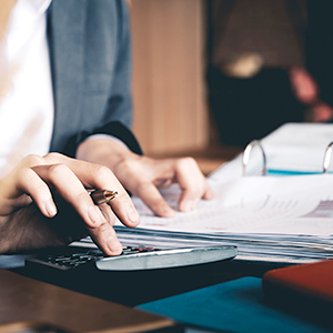 woman using a calculator at desk, with 3-ring binder and pen