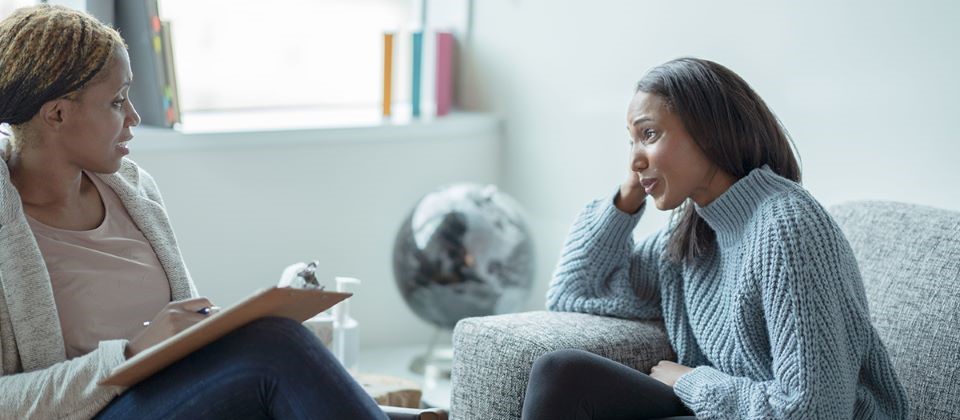 Two black women sitting across from each other on separate couches