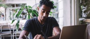 man taking notes while looking at a laptop