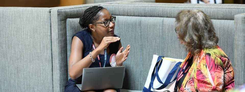 2 women sitting and speaking on a couch