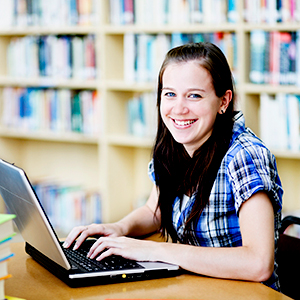 young woman looks up from working on laptop in library