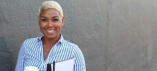 woman smiling at camera holding clipboard and coffee