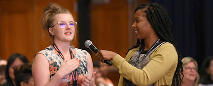 woman speaks into microphone while another woman holds it for her