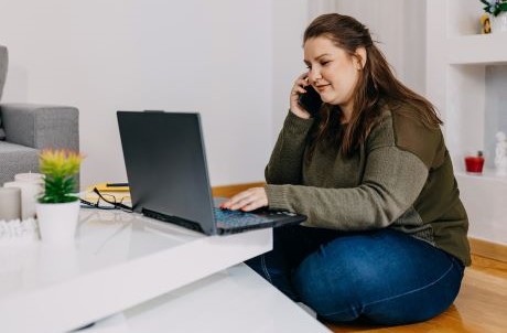 woman sitting in front of computer while talking on phone