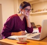 woman taking notes while looking at computer