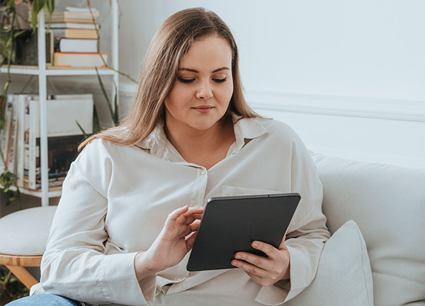 woman holding tablet sits on sofa