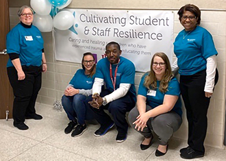 5 adults smiling in front of sign that reads Cultivating Student and Staff Resilience