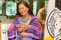 Suzanne Cross smiling with eyes closed, hands over heart, wearing purple quilt with lavender fringe