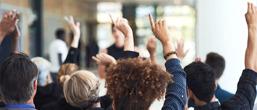 group of people seated in audience with hands raised