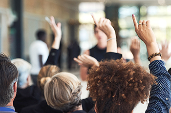 people at a meeting raise their hands