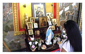 woman stands in front of homemade shrine with Christian icons