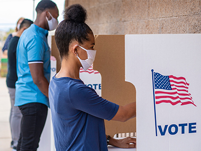 people at outdoor voting booths, wearing protective face masks