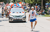 man kicks Hacky Sack in a parade; red, white and blue balloons