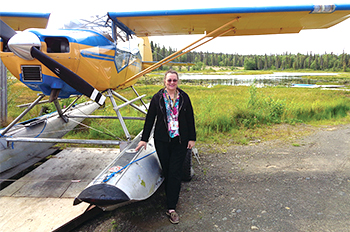 woman stands next to a two-seater airplane near a pine forest