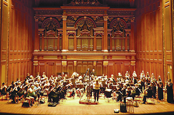 flute orchestra playing on stage with ornate organ pipes in background