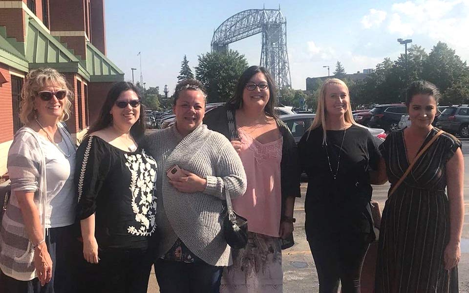 six women stand together outside