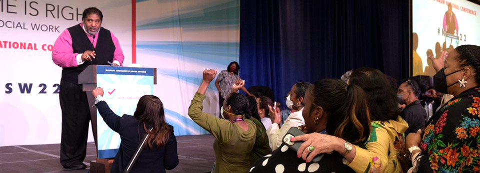 man at podium on stage, group of people cheering him on