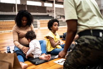 woman and two children sitting on floor while guard looks on