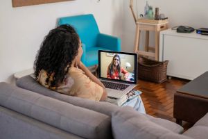person on couch facing laptop in online meeting