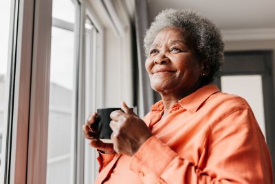 elderly person holding a mug and looking out the window