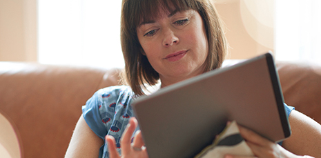 woman holding tablet sits on sofa