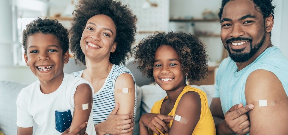 family with pointing to vaccine bandaids on their arms
