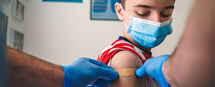 child in face mask getting a bandage on their arm by adult in surgical gloves