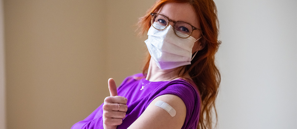 woman wearing medical face mask and adhesive bandage giving a thumbs up