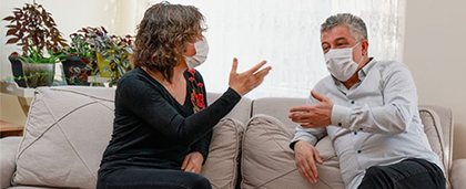 couple wearing face masks talks on sofa while woman with notepad observes