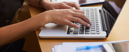 woman typing on laptop with cell phone and tablet on desk